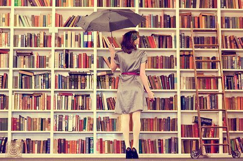 photographie couleur d'une très grande bibliothèque + femme tenant un parapluie qui regarde les centaines de livres